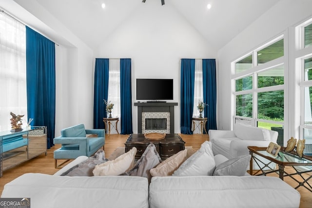 living room with light hardwood / wood-style floors, a tiled fireplace, and high vaulted ceiling