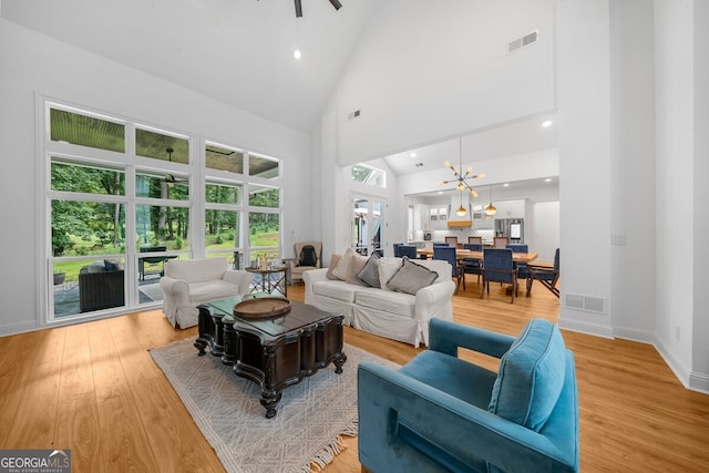 living room with a notable chandelier, light wood-type flooring, and high vaulted ceiling