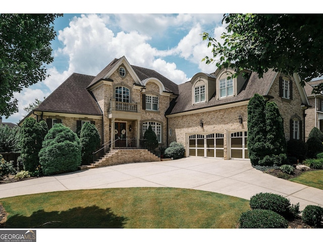 french country style house with a garage, concrete driveway, and brick siding