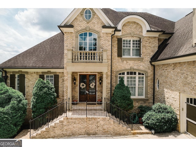 french provincial home featuring a shingled roof, french doors, and brick siding