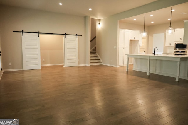 unfurnished living room featuring a barn door, sink, and dark wood-type flooring