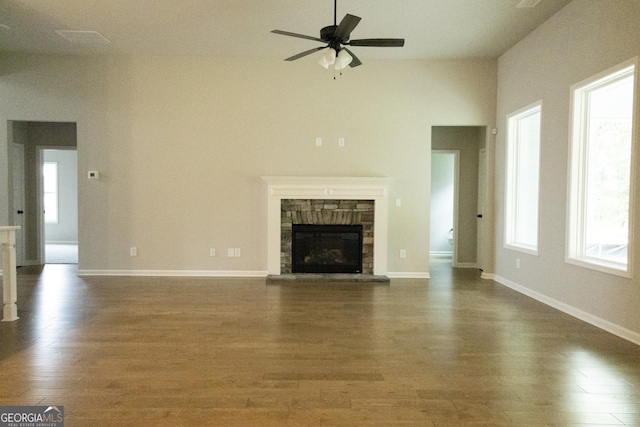 unfurnished living room with ceiling fan, a stone fireplace, dark hardwood / wood-style flooring, and a wealth of natural light