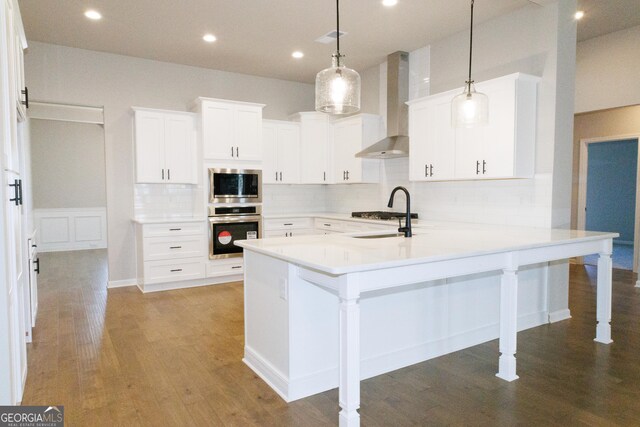 kitchen with wall chimney range hood, sink, decorative light fixtures, dark hardwood / wood-style flooring, and stainless steel appliances