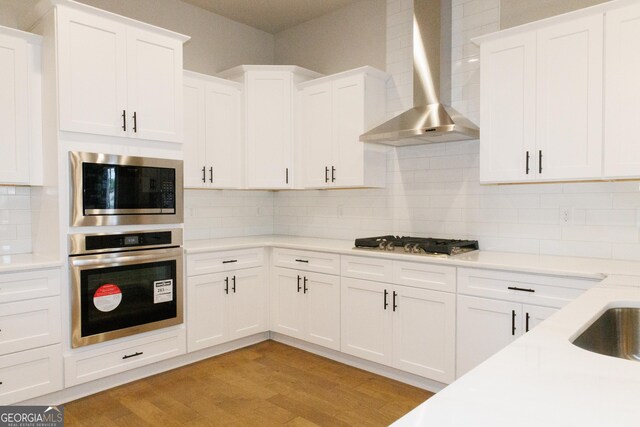 kitchen with appliances with stainless steel finishes, decorative light fixtures, white cabinetry, and wall chimney range hood