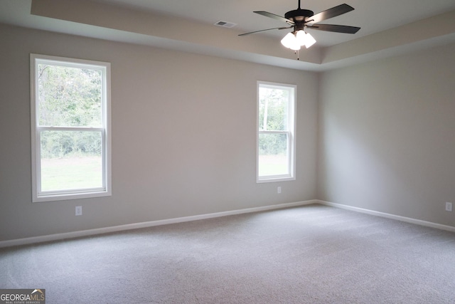 spare room with light carpet, a tray ceiling, and ceiling fan