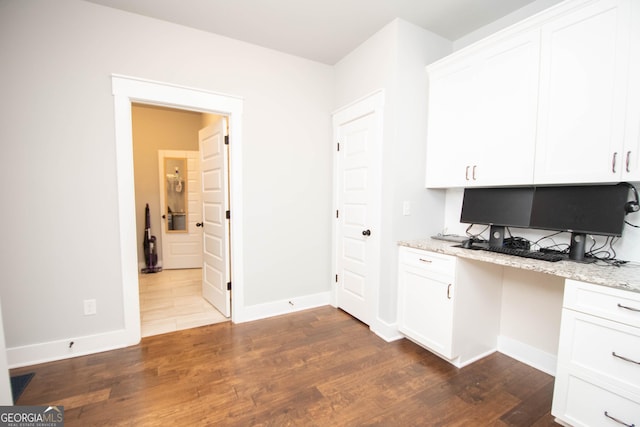 kitchen featuring white cabinets, dark hardwood / wood-style flooring, built in desk, and light stone counters