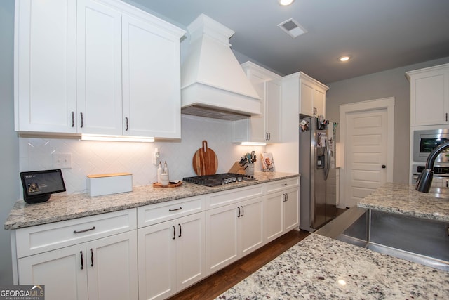 kitchen featuring premium range hood, dark hardwood / wood-style floors, light stone countertops, appliances with stainless steel finishes, and white cabinetry