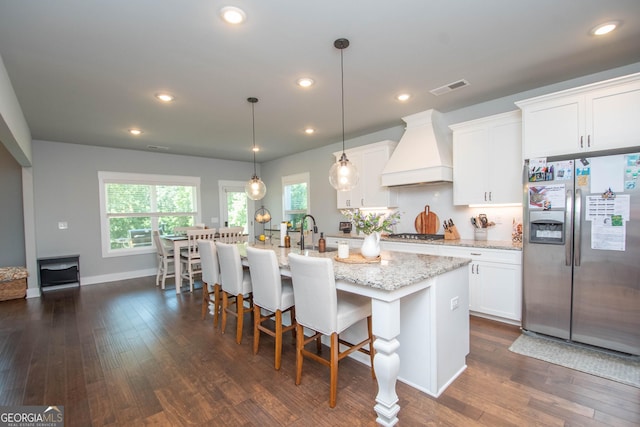 kitchen with visible vents, dark wood finished floors, custom range hood, appliances with stainless steel finishes, and a kitchen island with sink