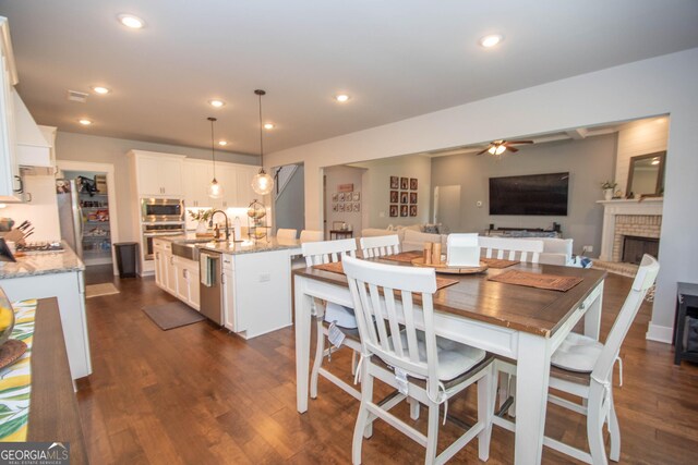 dining room with a fireplace, ceiling fan, dark wood-type flooring, and sink