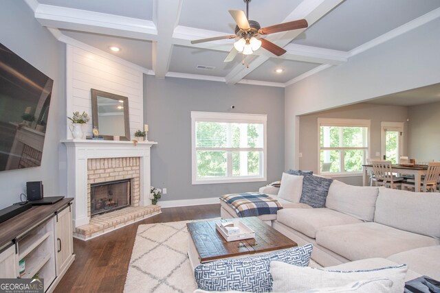 living room with a brick fireplace, coffered ceiling, ceiling fan, dark wood-type flooring, and beamed ceiling