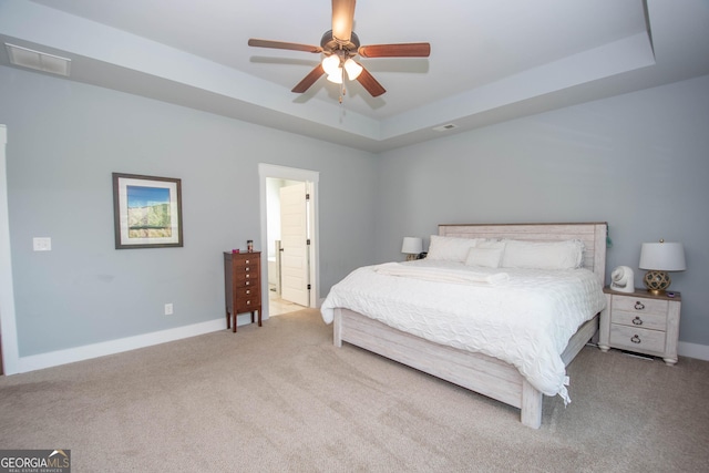 bedroom with a tray ceiling, connected bathroom, ceiling fan, and light colored carpet