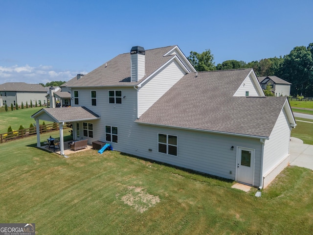 rear view of house featuring a chimney, a patio, a shingled roof, and a yard