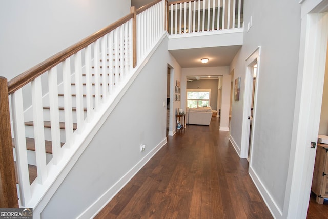 corridor featuring stairway, a high ceiling, baseboards, and dark wood-style flooring