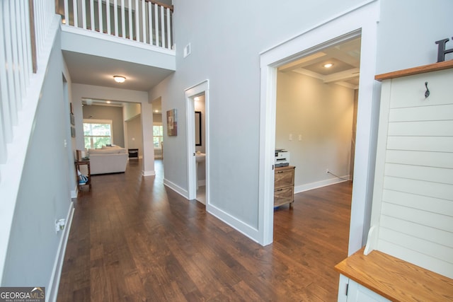 hall featuring visible vents, a high ceiling, baseboards, and dark wood-style flooring