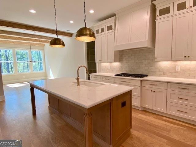 kitchen with a kitchen island with sink, backsplash, light wood finished floors, a sink, and gas cooktop