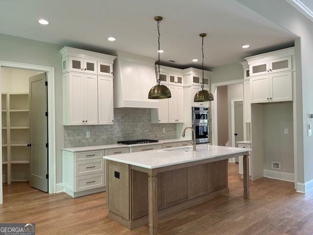 kitchen with a sink, cooktop, backsplash, white cabinetry, and light countertops