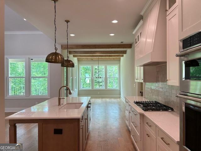 kitchen with light countertops, double oven, white cabinets, a sink, and gas cooktop