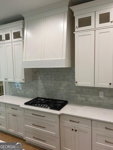 kitchen with glass insert cabinets, stainless steel gas cooktop, white cabinetry, and tasteful backsplash