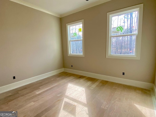 spare room with ornamental molding, light wood-style flooring, and baseboards