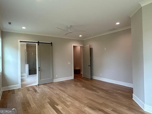 unfurnished bedroom with crown molding, a barn door, and baseboards