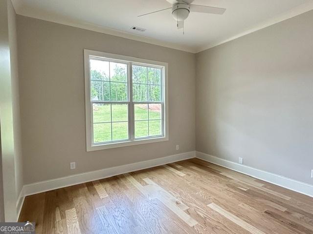 spare room with wood finished floors, ceiling fan, visible vents, and baseboards