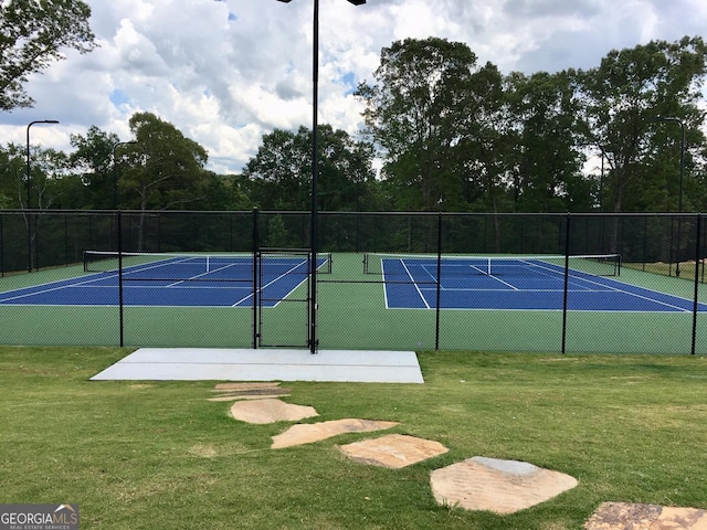 view of tennis court with fence and a yard