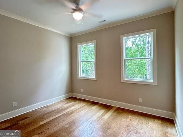 empty room featuring crown molding, a ceiling fan, visible vents, baseboards, and wood finished floors