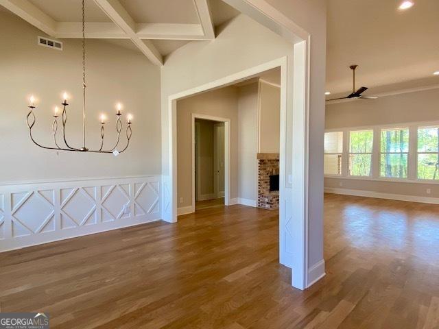 unfurnished dining area featuring wood finished floors, beamed ceiling, ceiling fan with notable chandelier, baseboards, and visible vents