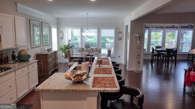 kitchen featuring white cabinetry, light stone counters, a wealth of natural light, a kitchen island, and decorative light fixtures