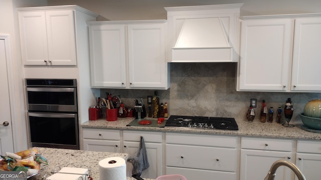 kitchen featuring stainless steel appliances, white cabinetry, custom range hood, and backsplash