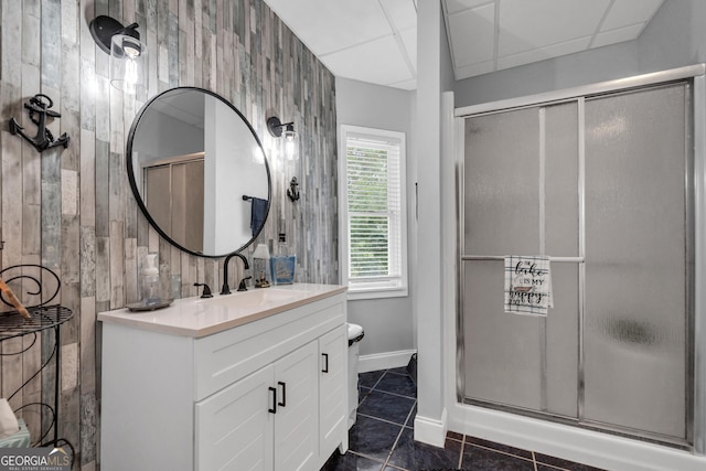 bathroom featuring a drop ceiling, wood walls, a shower with door, and vanity