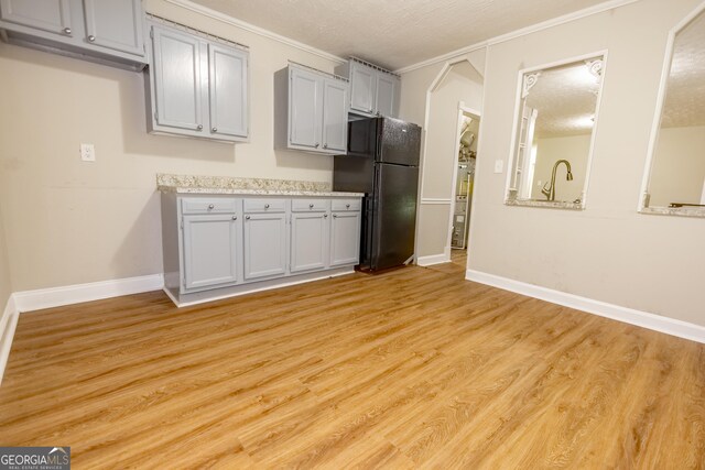 kitchen featuring gray cabinets, light wood-type flooring, a textured ceiling, black fridge, and ornamental molding