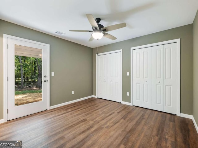 unfurnished bedroom featuring ceiling fan, access to outside, hardwood / wood-style floors, and multiple closets