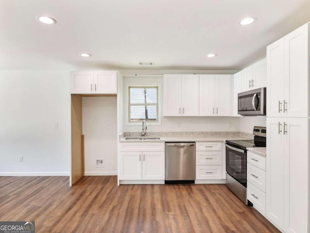 kitchen with appliances with stainless steel finishes, hardwood / wood-style flooring, white cabinetry, and sink