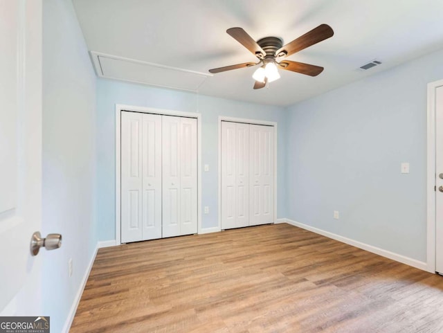 unfurnished bedroom featuring ceiling fan, two closets, and light wood-type flooring