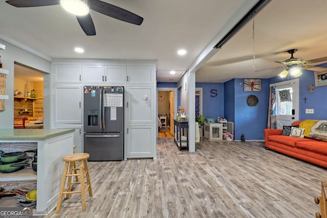 kitchen featuring ceiling fan, white cabinets, light wood-type flooring, a kitchen bar, and stainless steel fridge