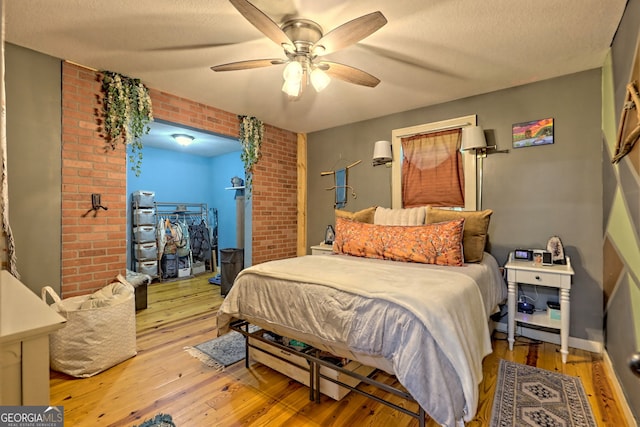 bedroom with light hardwood / wood-style floors, a textured ceiling, brick wall, and ceiling fan