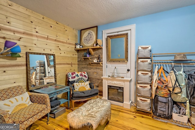 sitting room featuring wood walls, light hardwood / wood-style flooring, and a textured ceiling