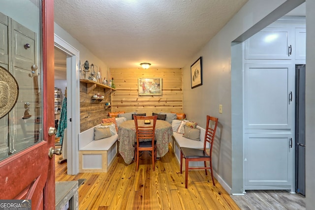 dining area with wooden walls, light wood-type flooring, and a textured ceiling