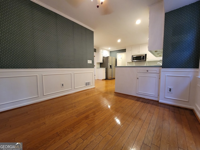 kitchen featuring crown molding, appliances with stainless steel finishes, light hardwood / wood-style floors, white cabinets, and kitchen peninsula