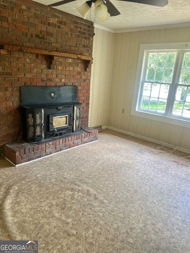 unfurnished living room with a textured ceiling, ceiling fan, a brick fireplace, brick wall, and a wood stove