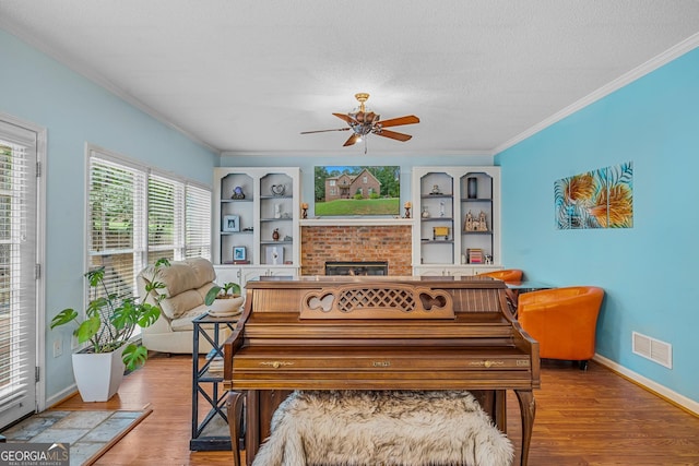 miscellaneous room with a brick fireplace, crown molding, wood-type flooring, and a textured ceiling