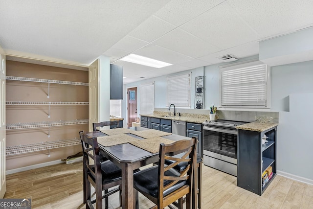 kitchen with sink, light hardwood / wood-style flooring, appliances with stainless steel finishes, light stone countertops, and a drop ceiling