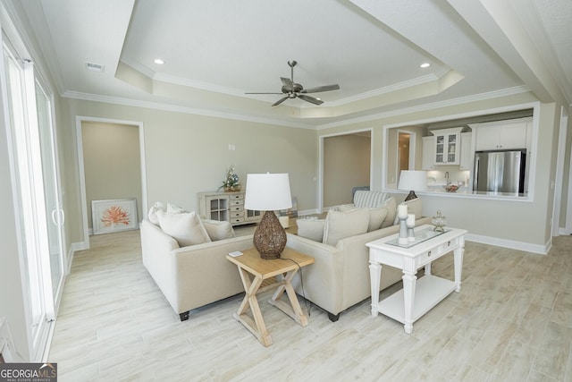 living area with visible vents, a raised ceiling, a ceiling fan, ornamental molding, and light wood-style floors