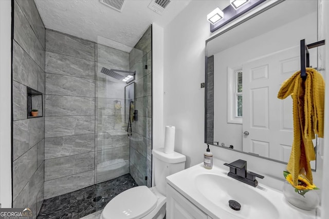 bathroom featuring vanity, toilet, a tile shower, and a textured ceiling