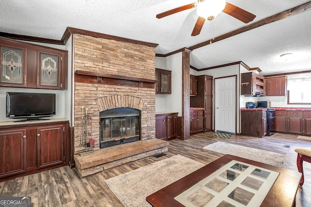 living room featuring ceiling fan, dark wood-type flooring, a fireplace, a textured ceiling, and ornamental molding