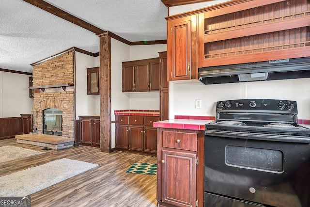 kitchen with hardwood / wood-style floors, a brick fireplace, black range with electric cooktop, ornamental molding, and lofted ceiling