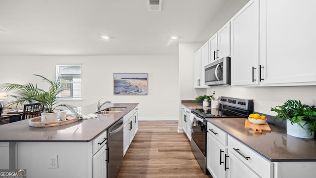 kitchen featuring appliances with stainless steel finishes, hardwood / wood-style floors, white cabinetry, sink, and a center island with sink