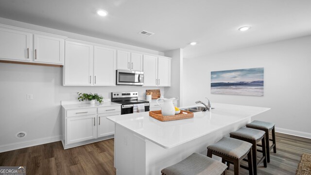 kitchen featuring visible vents, an island with sink, a sink, stainless steel appliances, and white cabinets