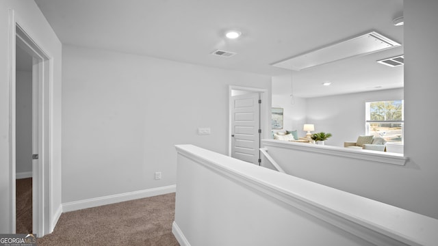 hallway featuring attic access, an upstairs landing, visible vents, and carpet floors